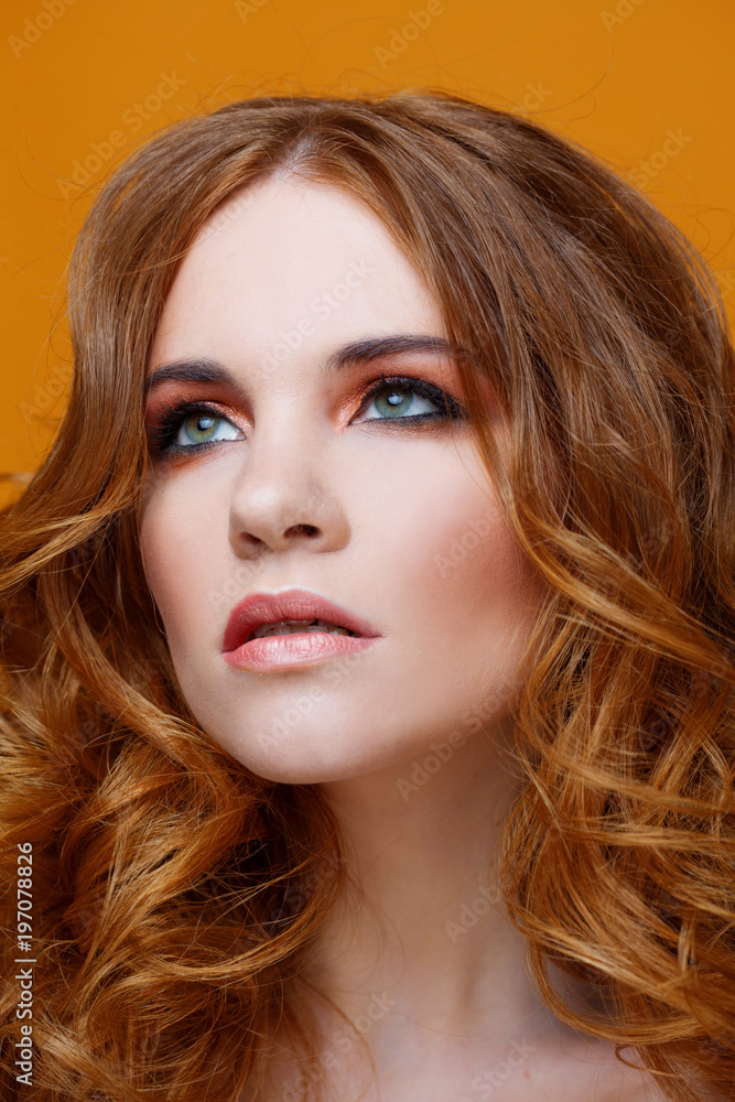 Fototapeta premium Beautiful redheaded girl with luxurious curly hair. Studio portrait on yellow background. Excellent hair