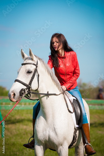  Woman sitting horse. Day. Full height. Red leather jacket