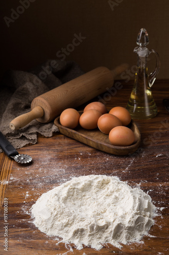 flourpot, eggs, rolling pin, olive oil in a jar on a wooden background photo