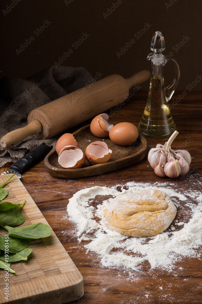 Fototapeta premium mug flour, eggs, rolling pin, olive oil in a jar on a wooden background, kneading
