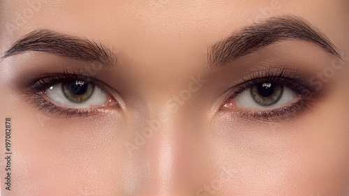Macro shot of beautiful eyes of the girl with beautiful eyebrows and long eyelashes. One eyebrow is raised. Brown shades in a make-up. Cosmetology, Spa, correction, injections