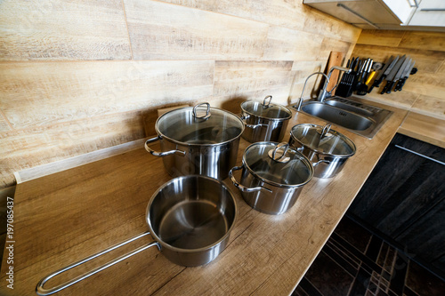 Image of kitchen ware. Set of shiny stainless steel saucepans big and small on wooden surface