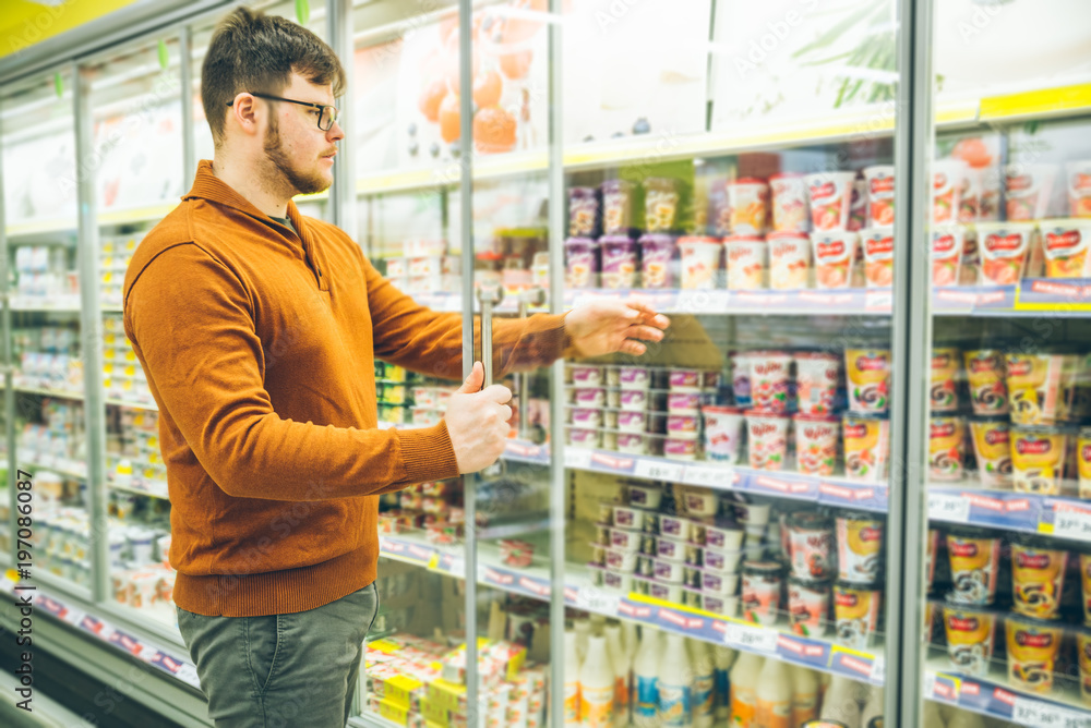 man takes yogurt from fridge. grocery shopping concept