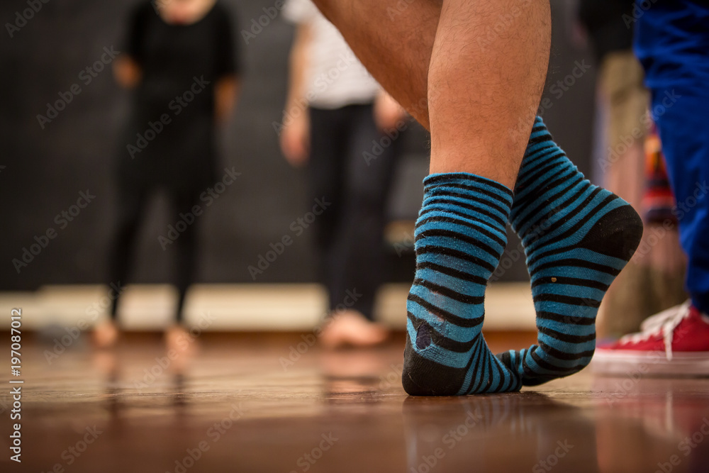 Naklejka premium Experienced teacher explaining a dance position. Feet standing closeup with blue and black striped socks in a room full of people. Concept: Teaching how to do it.