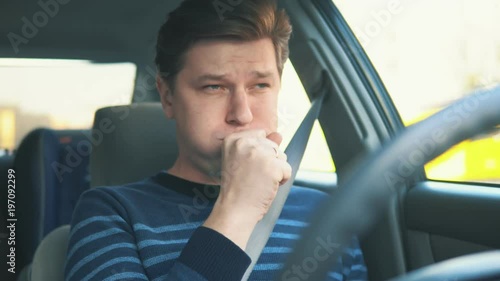 A young attractive man is coughing while driving in car