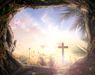 Empty tomb looking out to the cross on Golgotha with palm leaves at sunrise, concept of resurrection, Jesus Christ victory and Easter Sunday with copy space