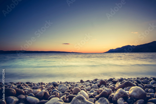Beautiful and colorful coastal sunset with island peninsula. Pebble beach in Croatia, Europe. Adriatic sea.