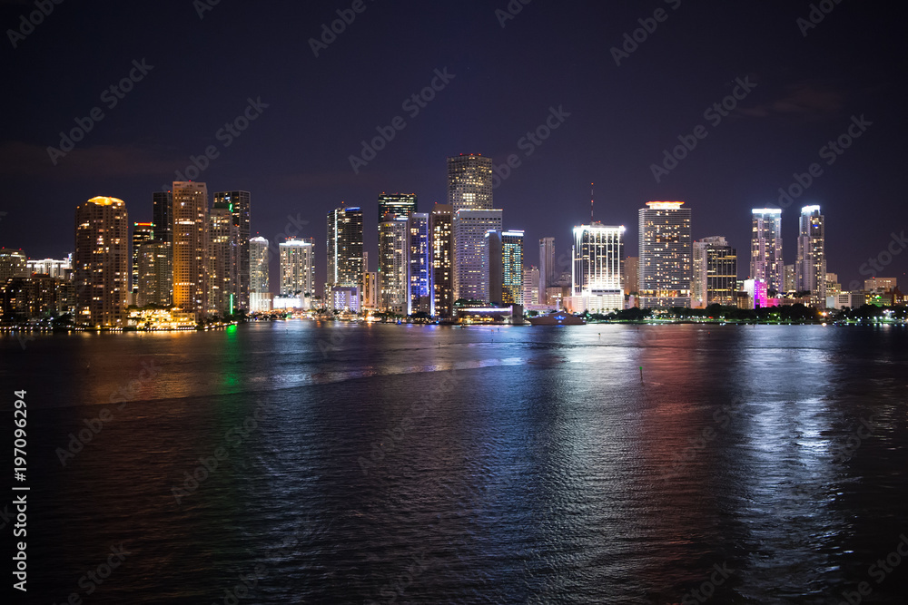 Naklejka premium Miami city skyline panorama at night, usa. Skyscrapers illumination reflect on sea water in dusk. Architecture, structure, design. Building, construction, development. Wanderlust, travel, discovery