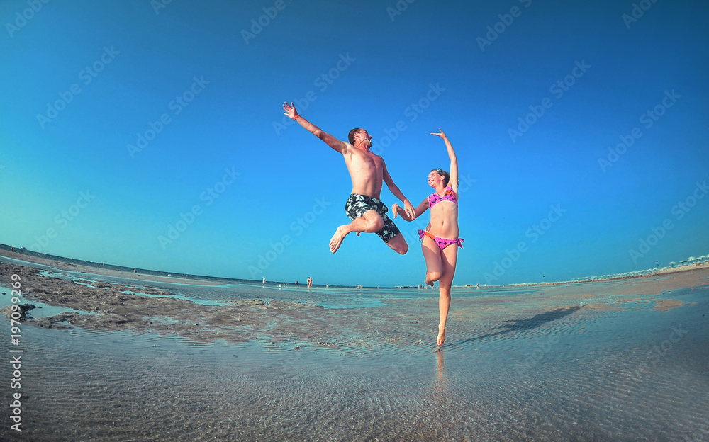 Happy young couple having beach fun on vacation honeymoon travel holidays. Caucasian woman and man playing playful enjoying love on date or honeymoon. Fisheye shot