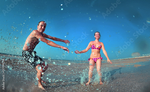 Happy young couple having beach fun on vacation honeymoon travel holidays. Caucasian woman and man playing playful enjoying love on date or honeymoon. Fisheye shot