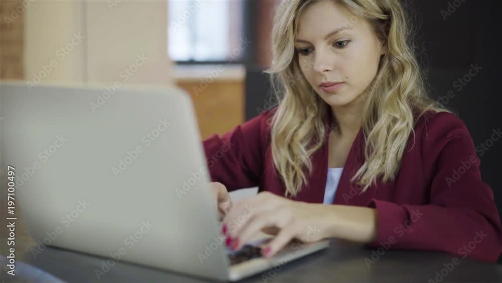 Attractive blonde woman in a red suit typing at her workplace in office. Left to right pan slow motion establishing shot Attractive blonde woman in a red suit typing at her workplace in office. Left to right pan slow motion establishing shot