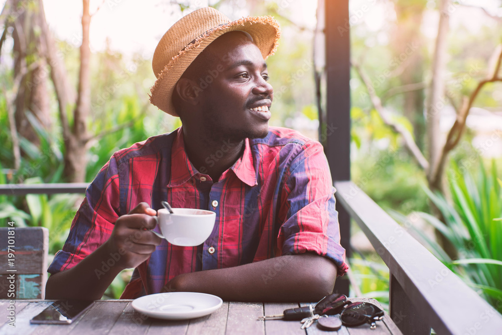 African american man holding a cup of coffee with key ,smartphone and green natural background. African american man holding a cup of coffee with key ,smartphone and green natural background.