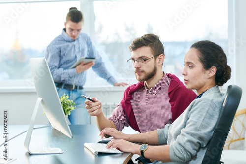 Caucasian female manager teaching young male employee while sitting at computer in modern office