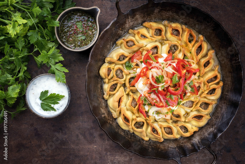 Traditional Armenian manti with mincemeat and paprika tomato salad as top view in a cast iron pan