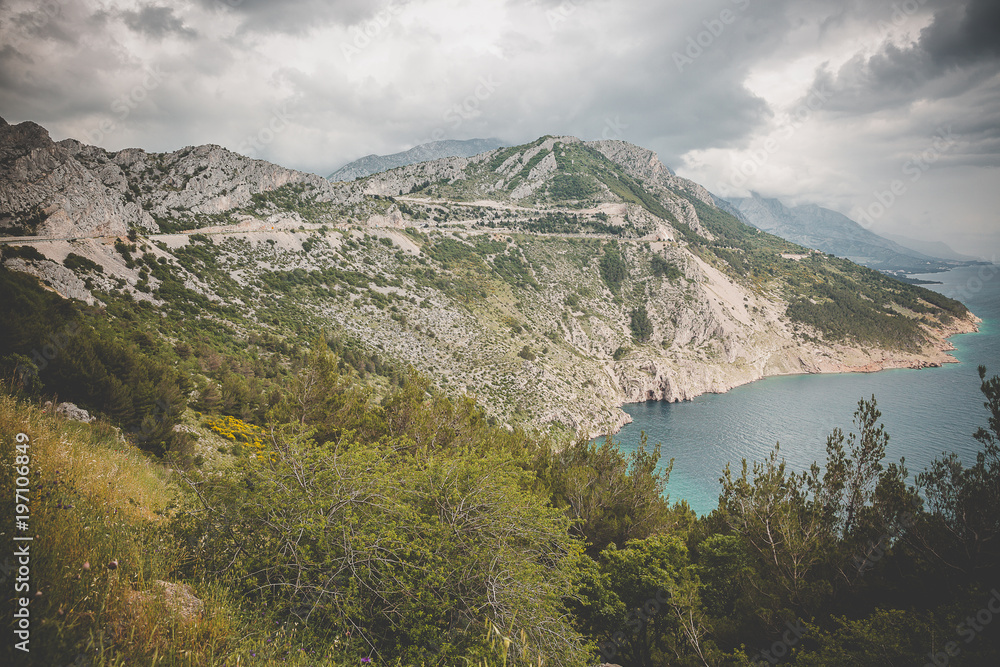 Aerial view on the cliff going down in the adriatic sea with dramatic cloudy sky, Croatia