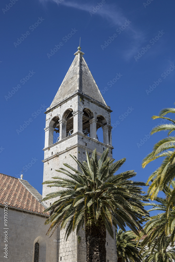 Bell tower of the Saint Dominican convent and church in Trogir, Croatia, surrounded by palm trees