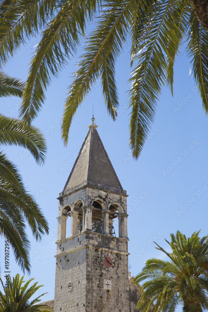Bell tower of the Saint Dominican convent and church in Trogir, Croatia, surrounded by palm trees
