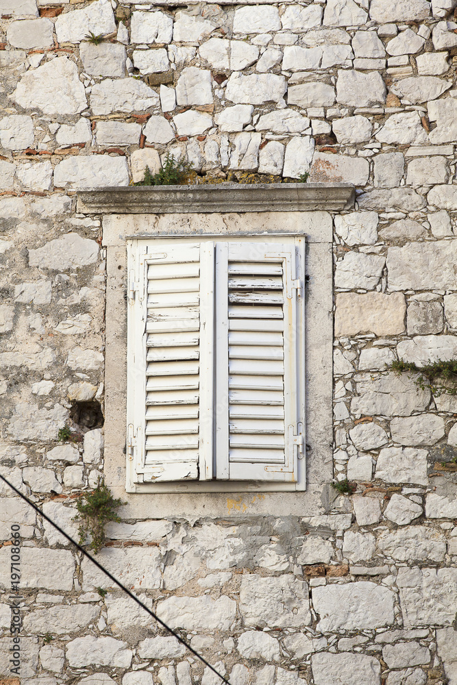 closed white wooden shutter of a old stone house