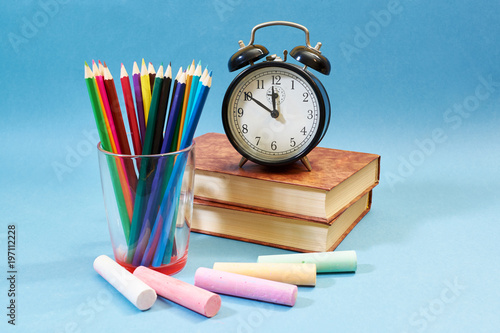background with books, alarm clock, pencils and chalks on blue background. Back to school concept.