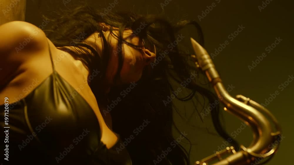 Young, beautiful, sexy, brunette woman dancing and playing golden saxophone on dark background . Shot on RED HELIUM Cinema Camera in slow motion. Young, beautiful, sexy, brunette woman dancing and playing golden saxophone on dark background . Shot on RED HELIUM Cinema Camera in slow motion.