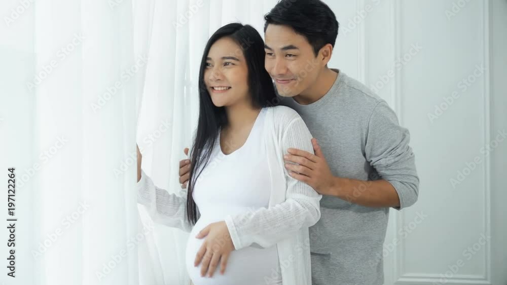 Young man and pregnant wife at the windows with curtains Young man and pregnant wife at the windows with curtains