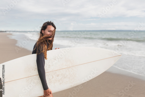 Young adorable woman with long hair and sportive tanned body, smiling and jogging with surf board on the beach in sunny summer day, ready for surfing. Wearing swimsuit