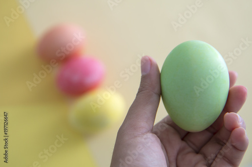 A hand holding a green pastel Easter egg with colorful background.