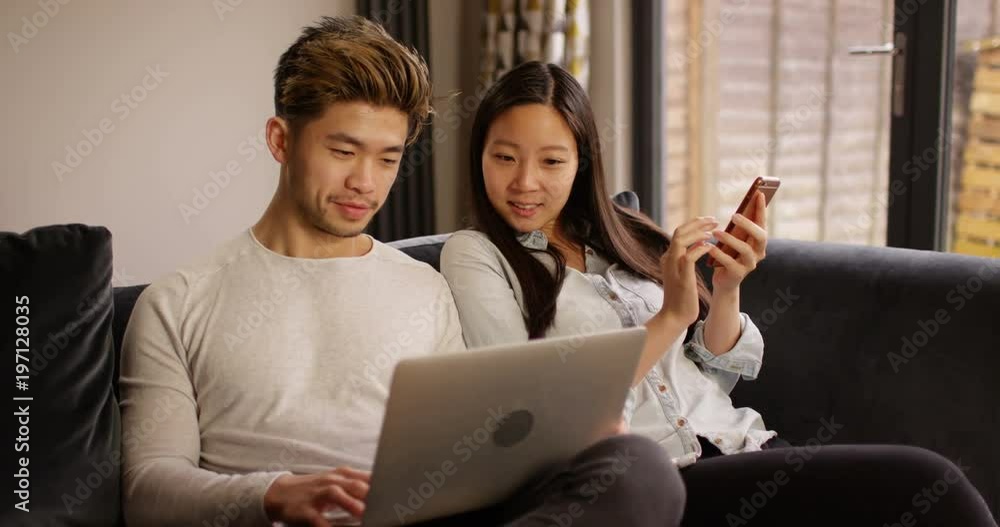 4K Happy young modern couple at home streaming media on laptop & smartphone. Slow motion. 4K Happy young modern couple at home streaming media on laptop & smartphone. Slow motion.