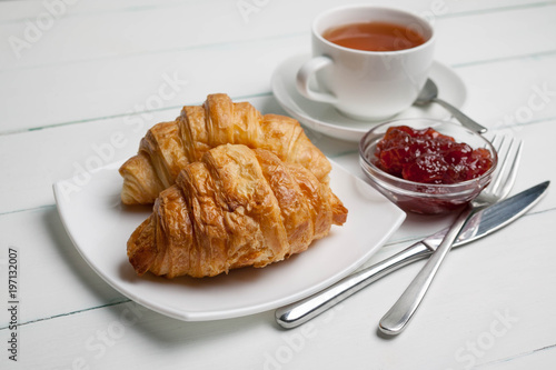 Croissants on a chopping board, strawberry jam and tea. Light breakfast