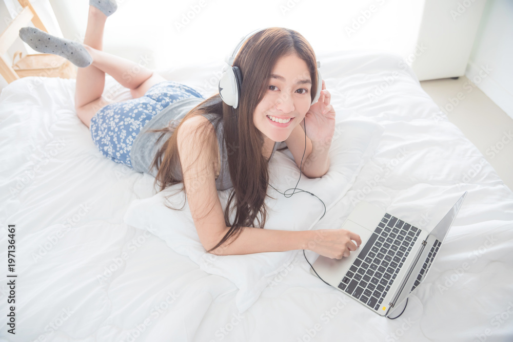 Beautiful asian woman lying on bed and using laptop computer with ...