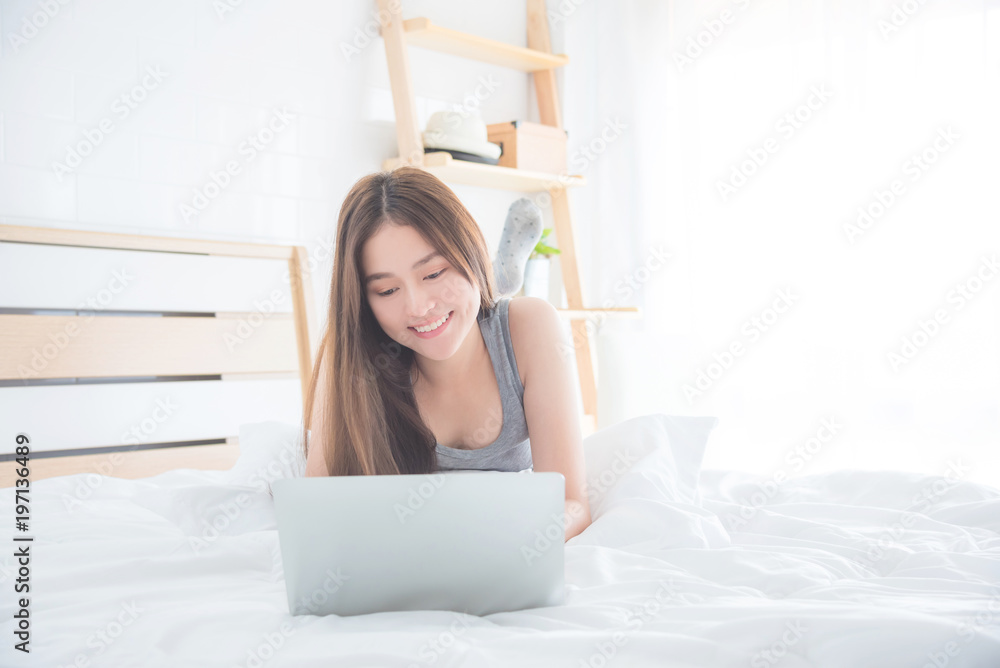 Beautiful asian woman lying on bed and using laptop computer with ...