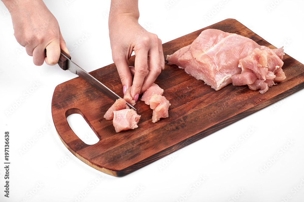 Cutting raw turkey meat with a kitchen knife on a cutting board isolated on white background