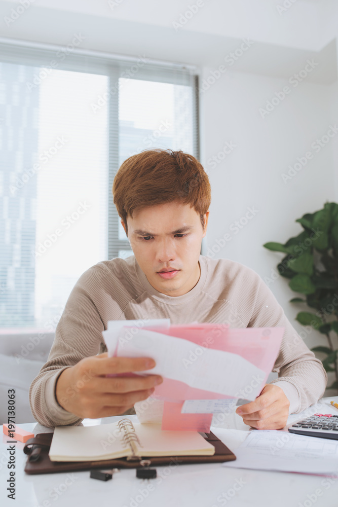 Asian young man counting using calculator and stress in problem with expenses.