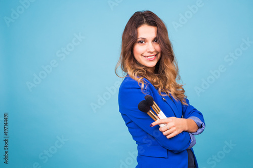 Close up portrait of make-up artist with brushes on blue background