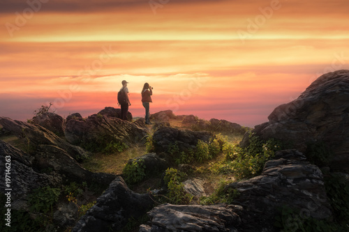Young couple stand on the peak of mountain watching beautiful sunset view. Travel and relationship concept