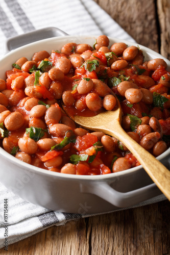 Stewed cranberry beans or borlotti in tomato sauce with herbs close-up in a bowl. vertical