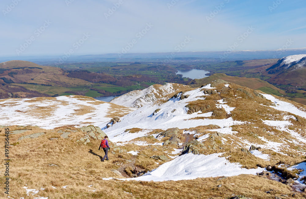 A female hiker descending from a snow covered Place Fell summit in the English Lake District.