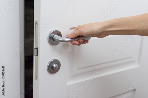The hand opens the door slightly. Detail of a white interior door with a chrome door handle and latch