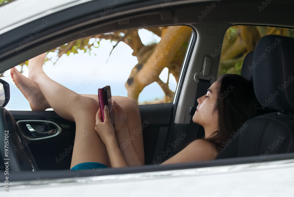 Teen girl using smartphone relaxing with legs out car window Teen girl using smartphone relaxing with legs out car window