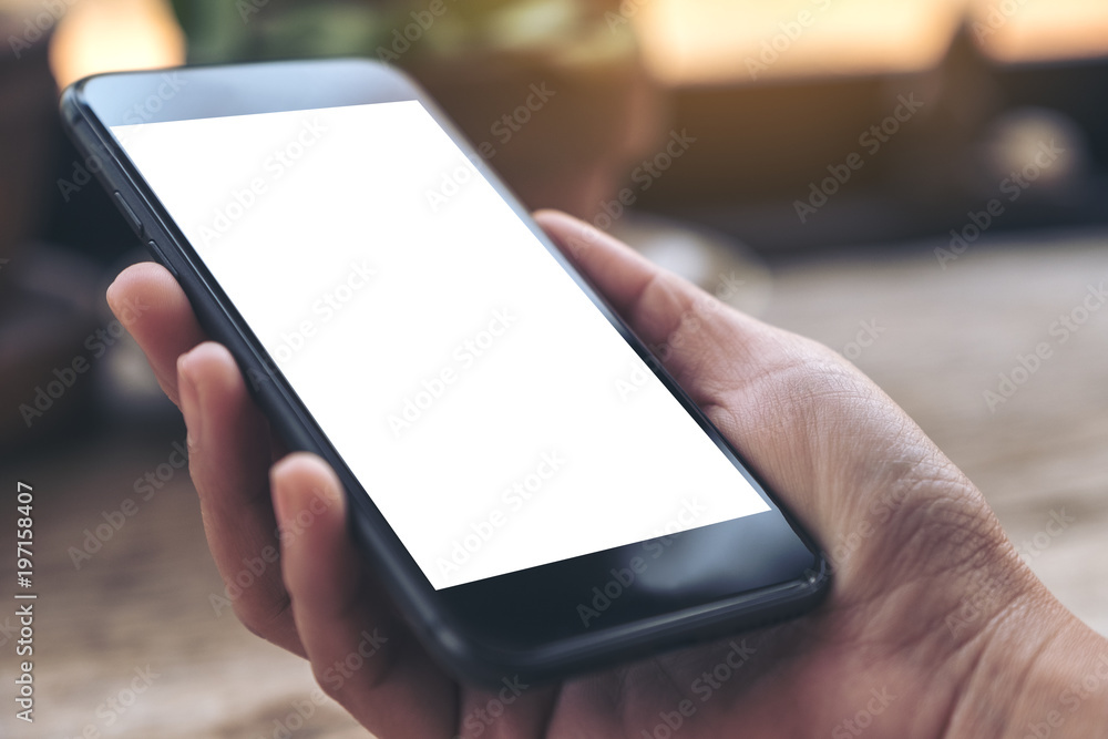 Mockup image of a hand holding black.mobile phone with blank white desktop screen on vintage wooden table in cafe Mockup image of a hand holding black.mobile phone with blank white desktop screen on vintage wooden table in cafe
