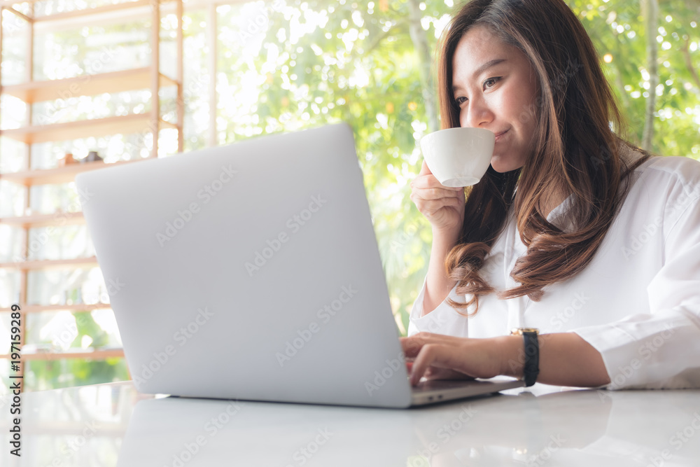 Closeup image of a beautiful Asian woman using laptop while drinking coffee in cafe Closeup image of a beautiful Asian woman using laptop while drinking coffee in cafe