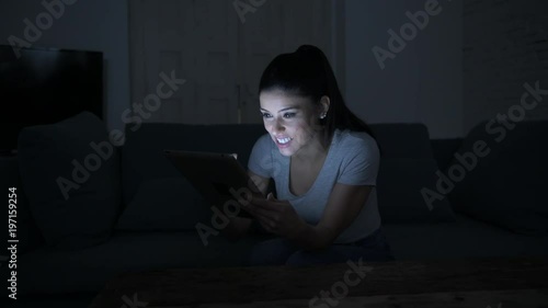 lateral pan shot of young beautiful happy and relaxed latin woman 30s lying on home couch late night using digital device laptop tablet pad 
