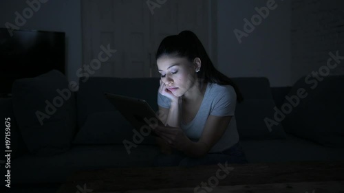 lateral pan latin woman 30s on home couch late night using digital device laptop tablet pad bored and tired
