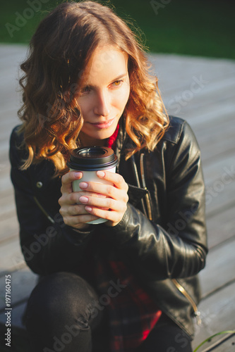 Young beautiful woman in a black leather jacket drinking coffee