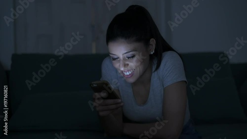 young attractive and relaxed hispanic 30s woman with mobile phone smiling happy using dating app late night in internet social media addiction concept
