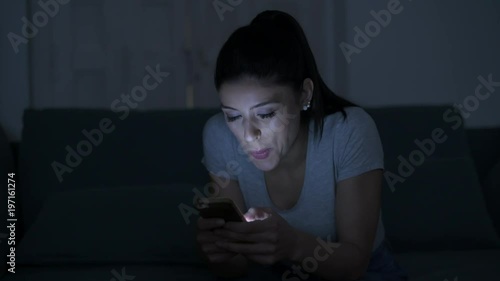 young attractive and relaxed hispanic 30s woman with mobile phone smiling happy using dating app late night in internet social media addiction concept
