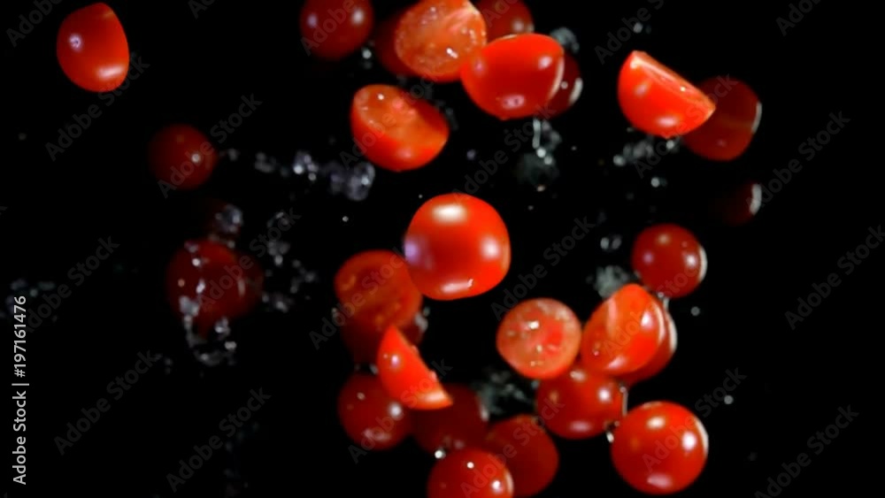 Whole and halves of tomatoes with water bouncing against to the camera on a black background in slow motion Whole and halves of tomatoes with water bouncing against to the camera on a black background in slow motion