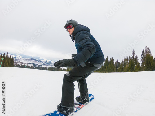 A young man in sports glasses is riding a snowboard in the mountains in Transcarpathia