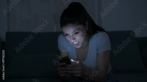 young attractive and relaxed hispanic 30s woman with mobile phone smiling happy using dating app late night in internet social media addiction concept
