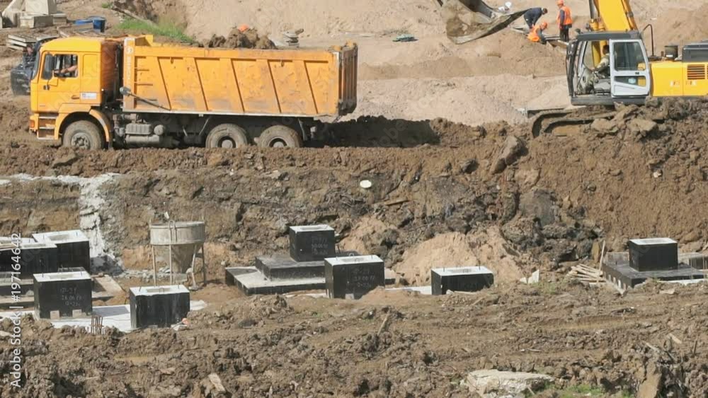 Excavator with its bucket pushes yellow dump truck from the mud on a construction site in the summer season Excavator with its bucket pushes yellow dump truck from the mud on a construction site in the summer season